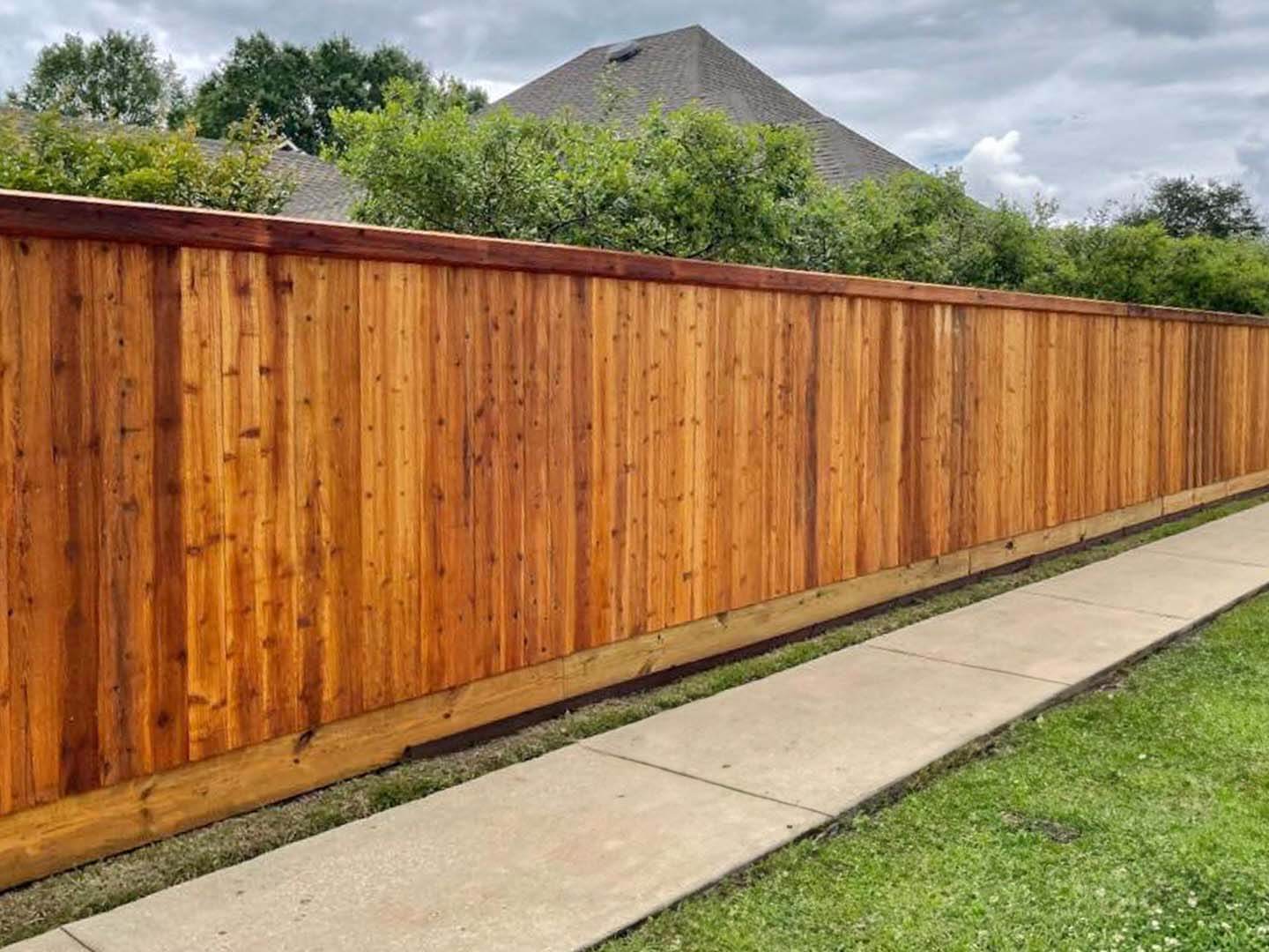 Full privacy wood fence with beveled edge top cap trim installed around a yard