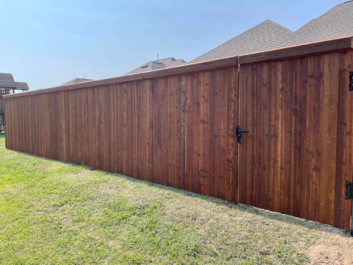 Full privacy wood fence with beveled edge top cap trim installed around a yard