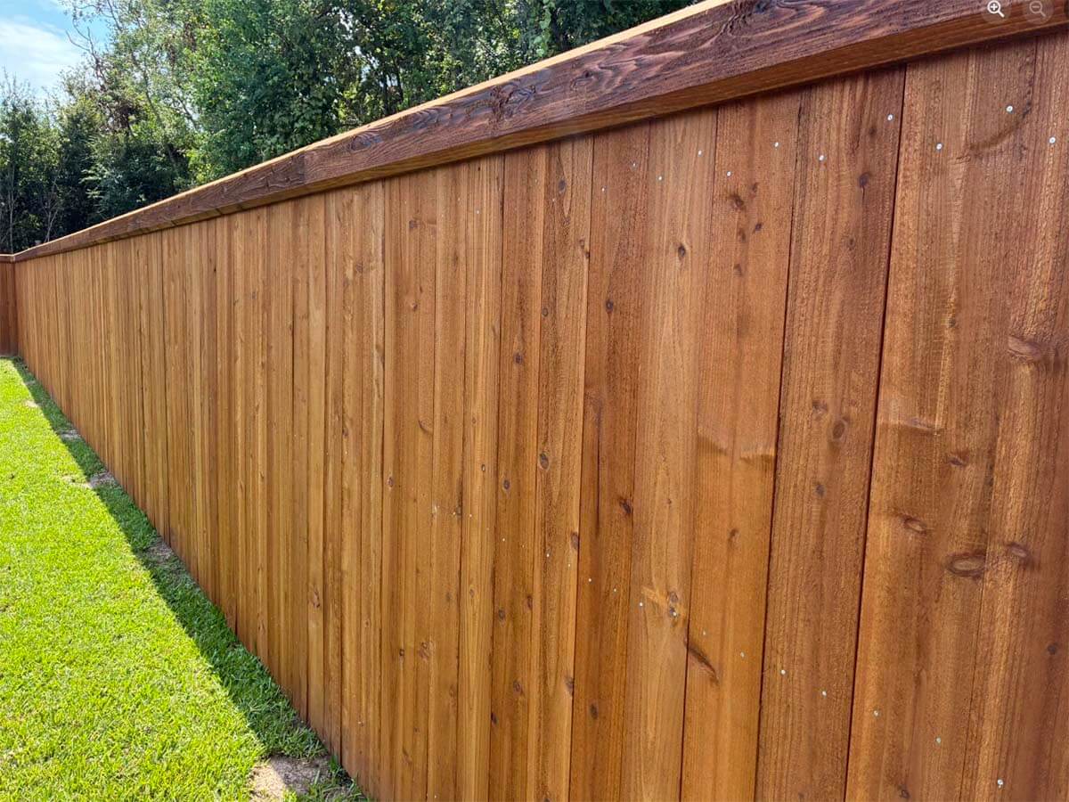 Full privacy wood fence with beveled edge top cap trim installed around a yard